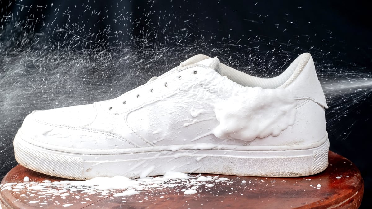 White leather sneakers being sprayed with cleaning foam
