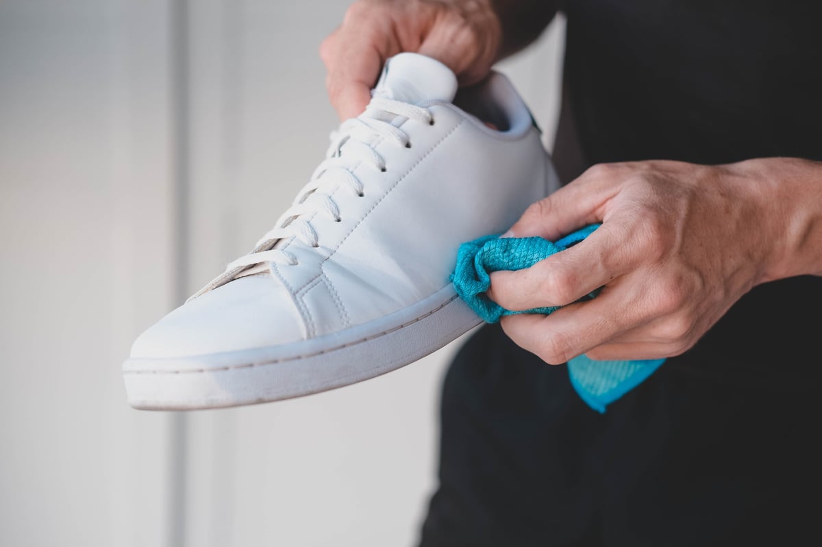 A pair of white sneakers being cleaned of dirt by hand
