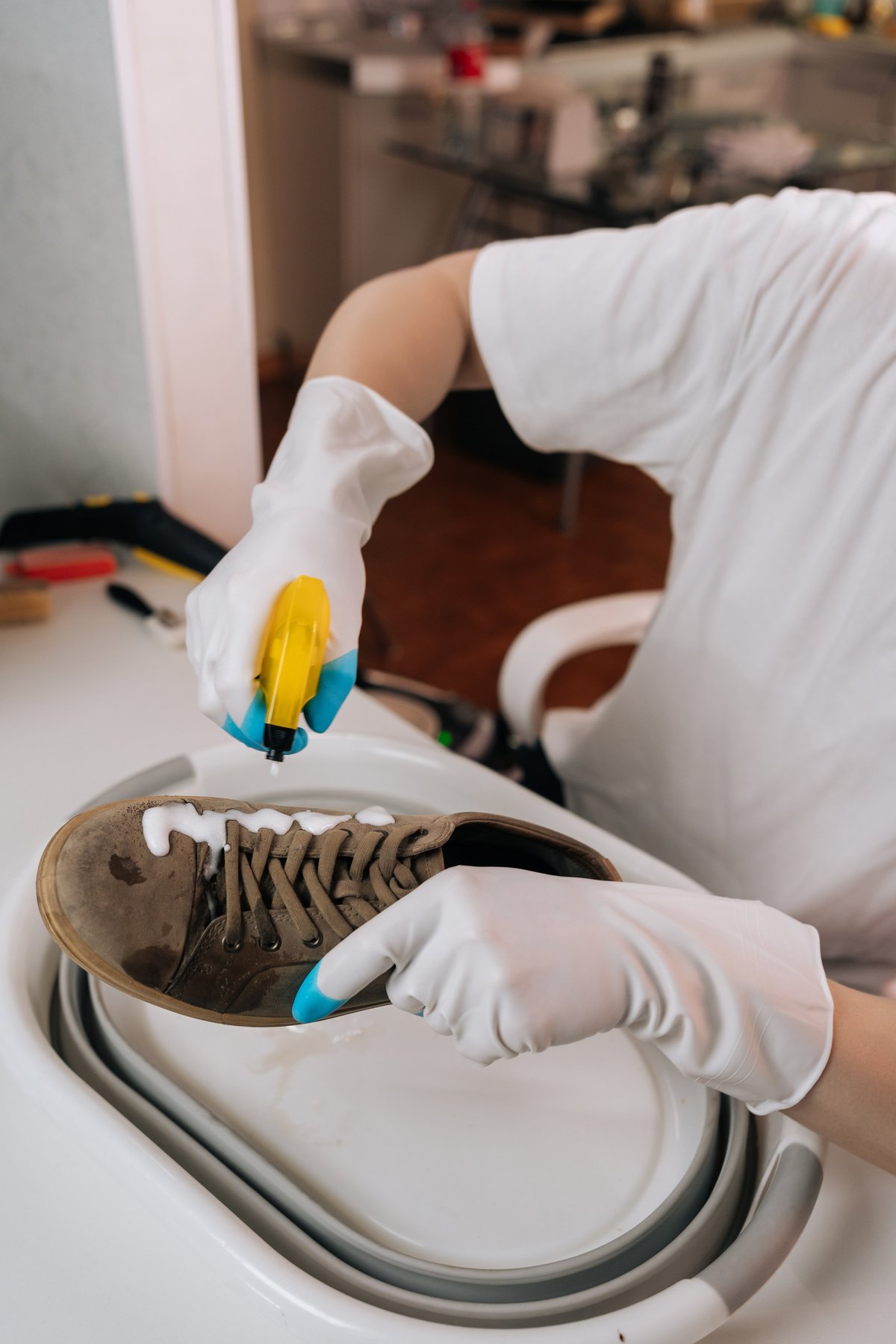 Hands in gloves spraying cleaning foam onto a suede sneaker in the studio